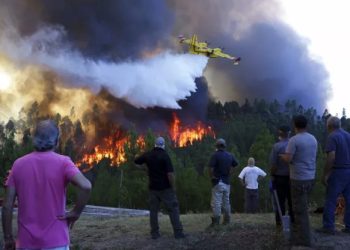 foto: FILE - Villagers watch a firefighting plane drop water to stop a raging forest fire from reaching their homes in Chao de Codes, central Portugal, Aug. 2017.